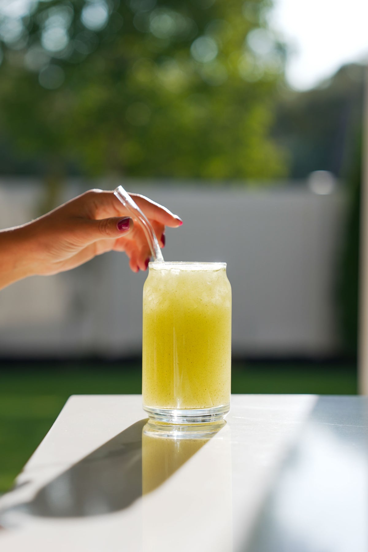 Hand resting on the straw of a glass of Daily Greens outdoors