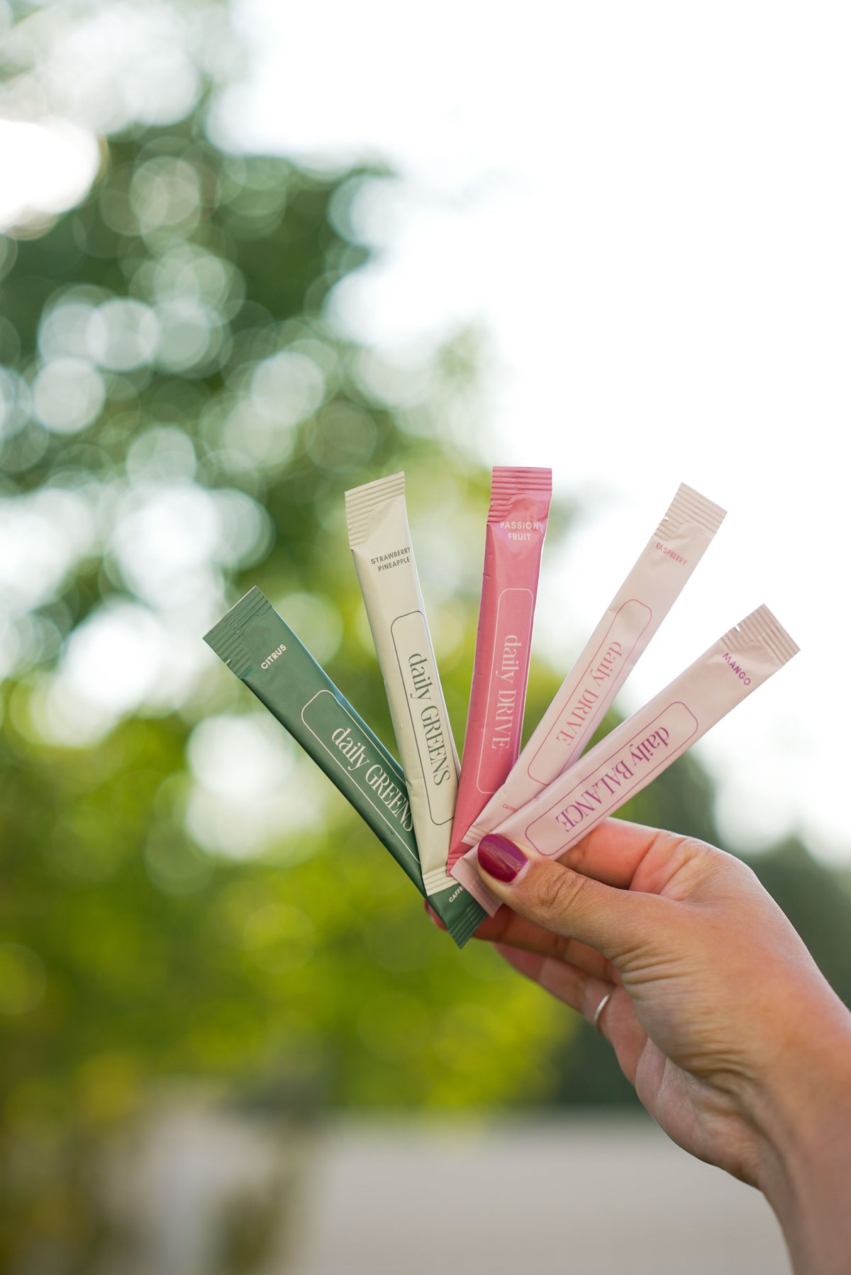 Hand fanning five dailyRU stick packs against sunlit trees